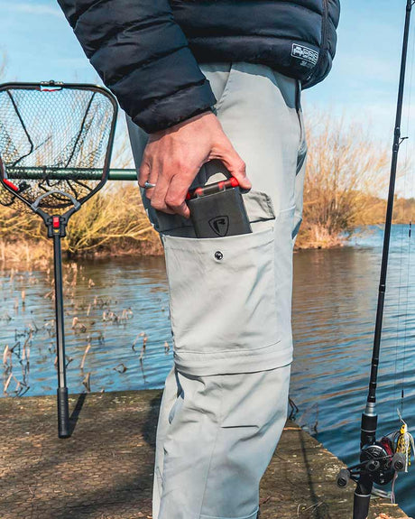 Pantalón desmontable Fox Rage color gris claro, ideal para pesca, con bolsillo seguro, en entorno natural.